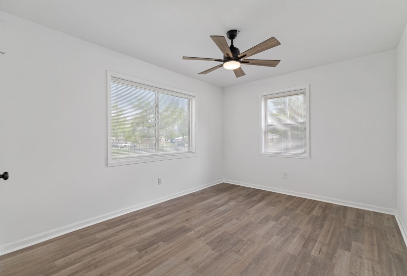Spacious room featuring wood-finish flooring, white walls, and a modern ceiling fan with light fixture