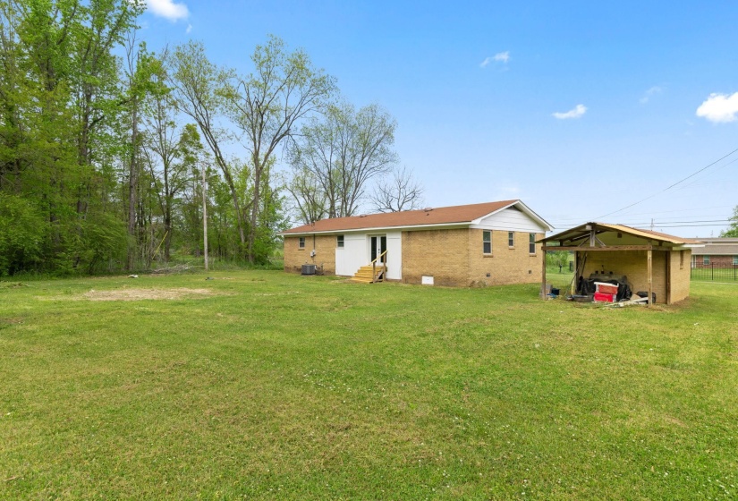 Expansive grassy yard with a brick exterior home featuring white trim, a brown roof, and a rear white door with steps