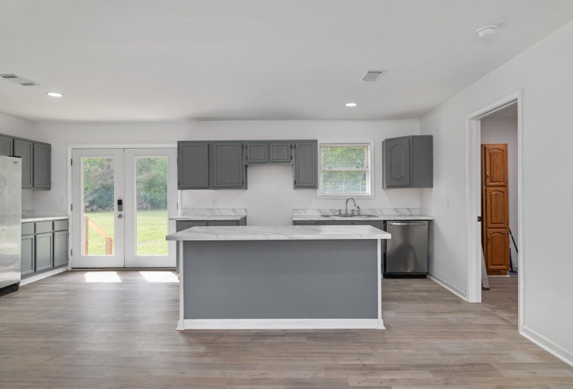 Contemporary kitchen featuring a central island with white countertop, grey cabinetry, stainless steel appliances, and light wood-finish flooring