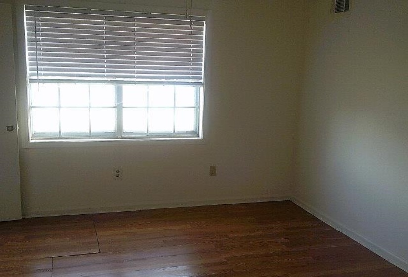 Room featuring wood-finish flooring, a double-hung window with horizontal blinds, and neutral wall paint