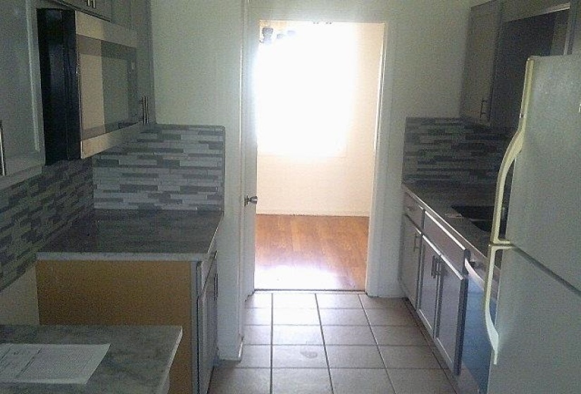 Galley kitchen featuring grey cabinetry, stainless steel microwave, stone-finish countertops, subway tile backsplash, and ceramic tile flooring