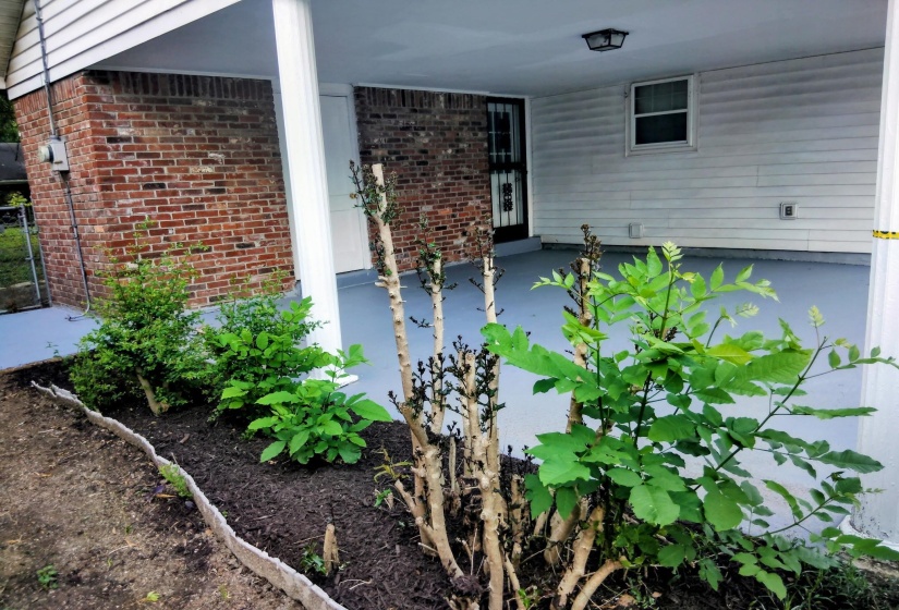 Covered carport featuring a painted concrete floor, white siding, and a brick exterior wall
