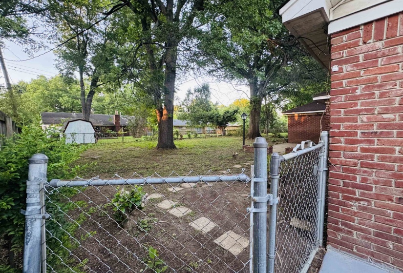Spacious backyard featuring mature trees, a chain-link fence, and a stepping stone path