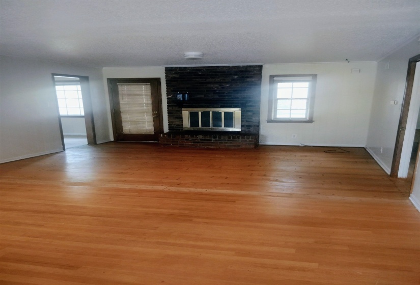 Living area featuring wood-finish flooring, a brick-front fireplace with a metal insert, and multiple windows