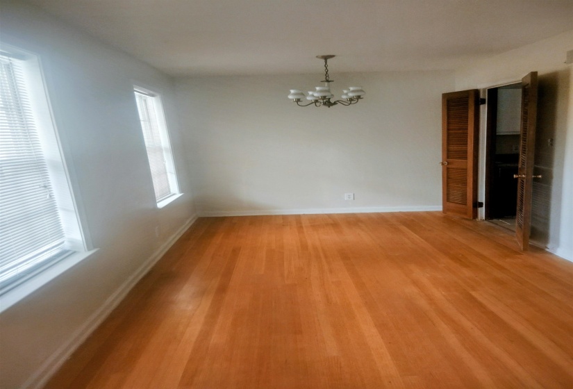 Spacious room featuring hardwood flooring, multiple windows with blinds, a chandelier light fixture, and louvered bifold doors
