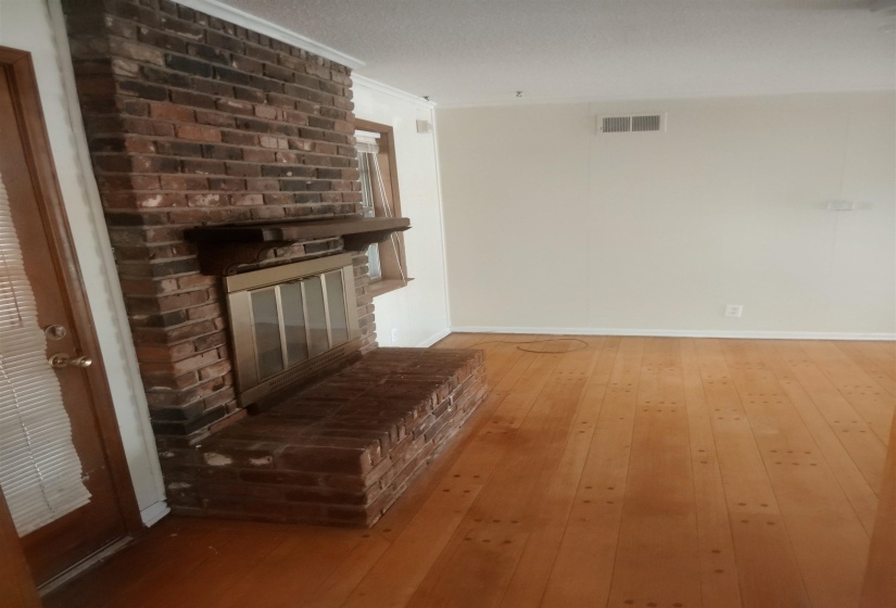 Brick fireplace with hearth, wood-finish flooring, white crown molding, and neutral wall paint