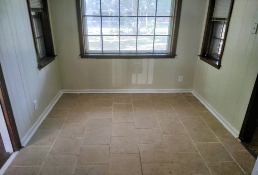 Neutral-toned tile flooring, three large windows with dark wood trim, painted paneling on side walls, and light-colored wall paint