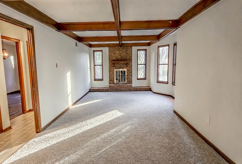 Spacious room with exposed wood ceiling beams, a brick fireplace with hearth, and multiple windows