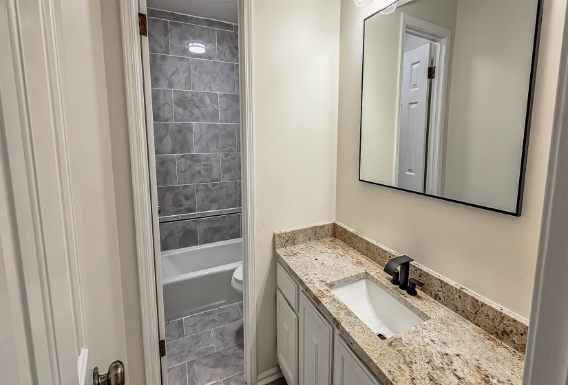 Bathroom vanity featuring a light-toned granite countertop, undermount sink, and matte black faucet