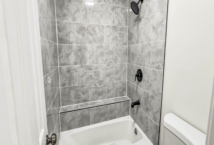 Bathtub with gray subway tile surround and built-in ledge, featuring matte black fixtures