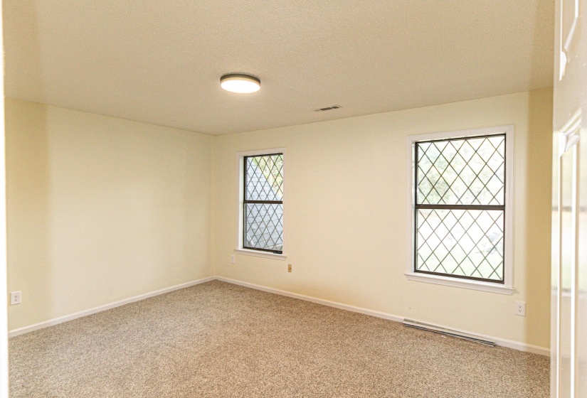Spacious room featuring two diamond-patterned windows, light-colored walls, and textured carpeting