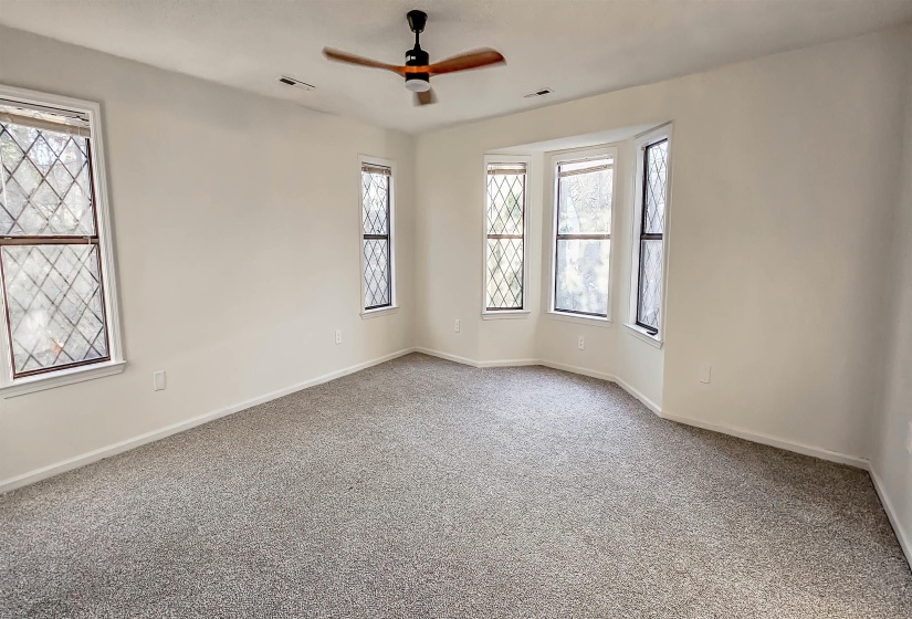 Spacious room featuring light-colored walls, gray carpeting, and multiple windows with diamond-patterned grilles