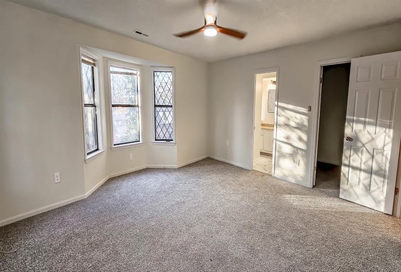 Spacious room with gray carpet, a bay window with decorative grilles, and a ceiling fan