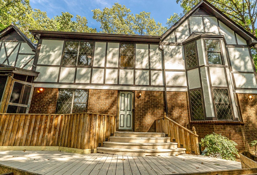 Tudor-style architecture featuring brick and half-timbering, a wooden deck, and a screened-in porch