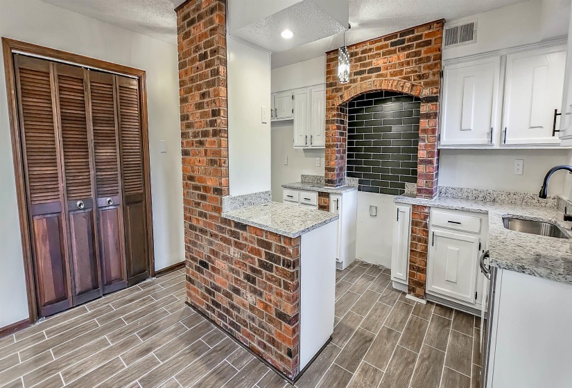 Kitchen featuring a brick archway with dark subway tile, white cabinetry, and light-toned countertops