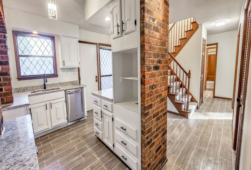 Kitchen and entryway featuring wood-look tile flooring, white cabinetry, granite countertops, and a full brick pillar