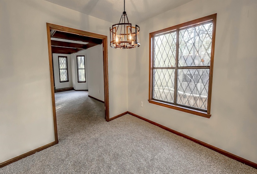 Inviting interior space featuring a contemporary chandelier, diamond-pane windows with wood trim, neutral wall tones, and plush carpet flooring