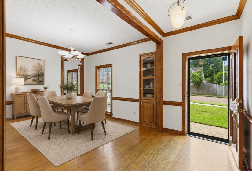 Dining area featuring wood-finish flooring, light walls with wood trim, a built-in wood display cabinet, and a multi-light chandelier. Furniture is virtually staged.