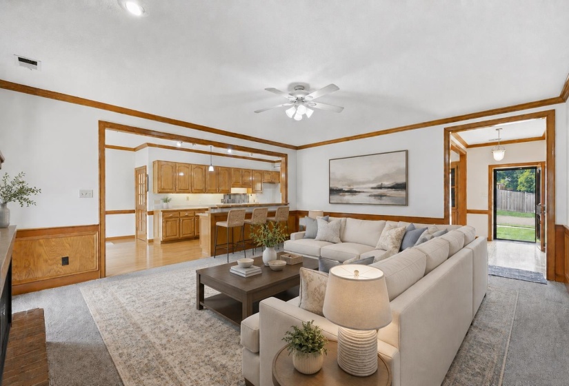 Spacious living area featuring carpet flooring, wood-paneled wainscoting, and crown molding. Furniture is virtually staged.