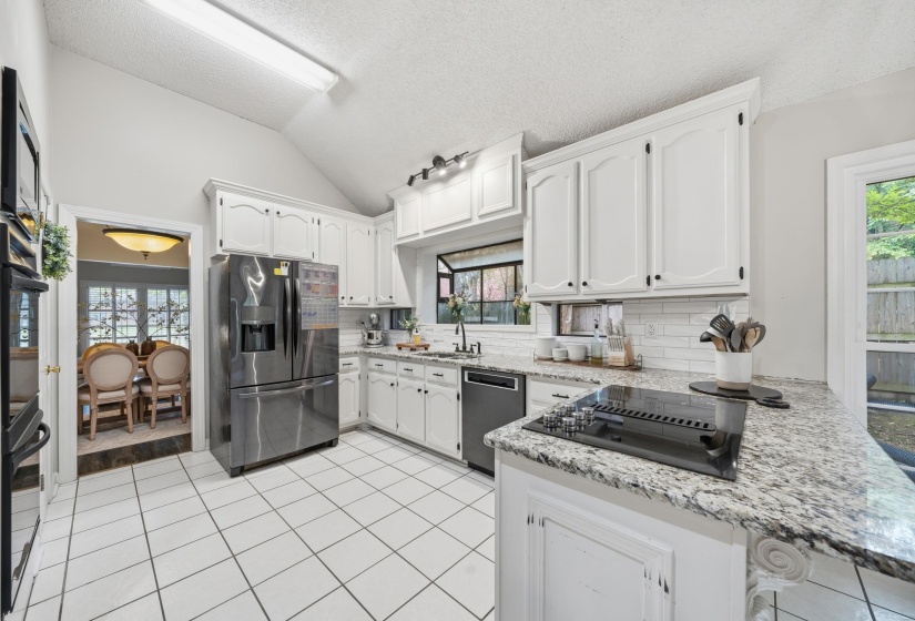 White kitchen featuring granite countertops, white subway tile backsplash, white cabinetry, and stainless steel appliances
