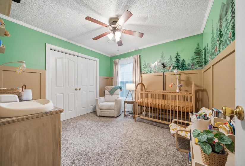 Carpeted room featuring a ceiling fan with integrated lighting, bi-fold closet doors, crown molding, and wainscoting