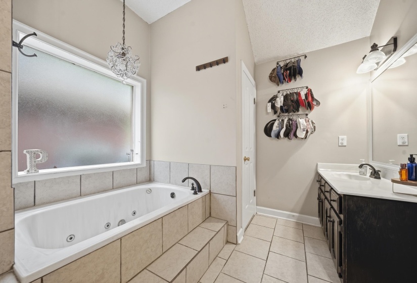 Bathroom featuring a tiled jetted tub with a frosted window, a vanity with an integrated sink, and an overhead light fixture