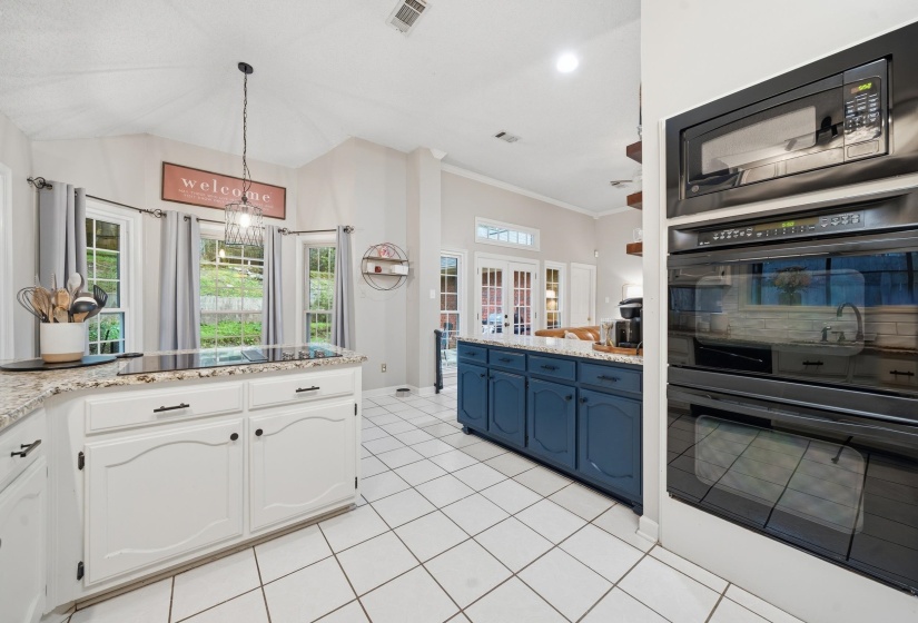 Expansive kitchen featuring a white tile floor, white cabinetry, a built-in cooktop, a double oven, and a contrasting blue island with granite countertops