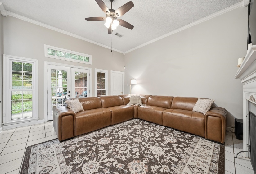 Living area featuring a vaulted ceiling with a ceiling fan, white tile flooring, French patio doors, and a decorative fireplace with a white mantel