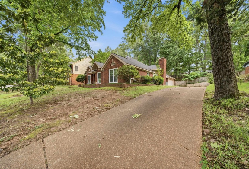 Brick exterior residence with a concrete driveway, surrounded by mature trees and established landscaping