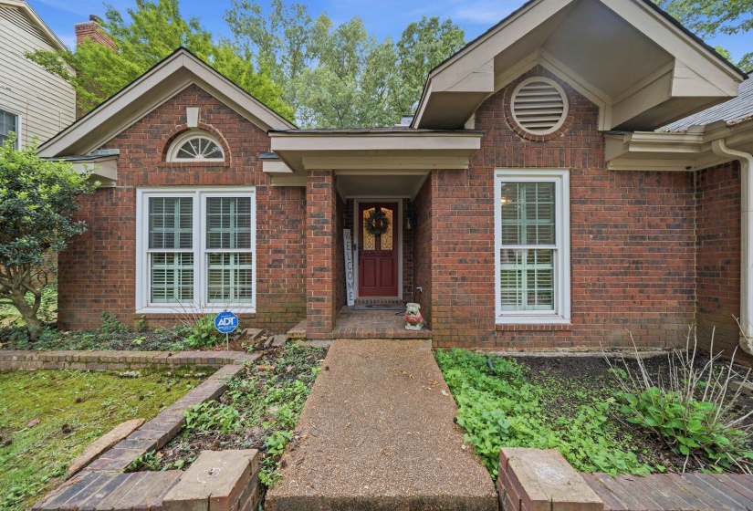 Brick exterior featuring a red entry door, white trim windows, a semicircular transom window, and an arched vent
