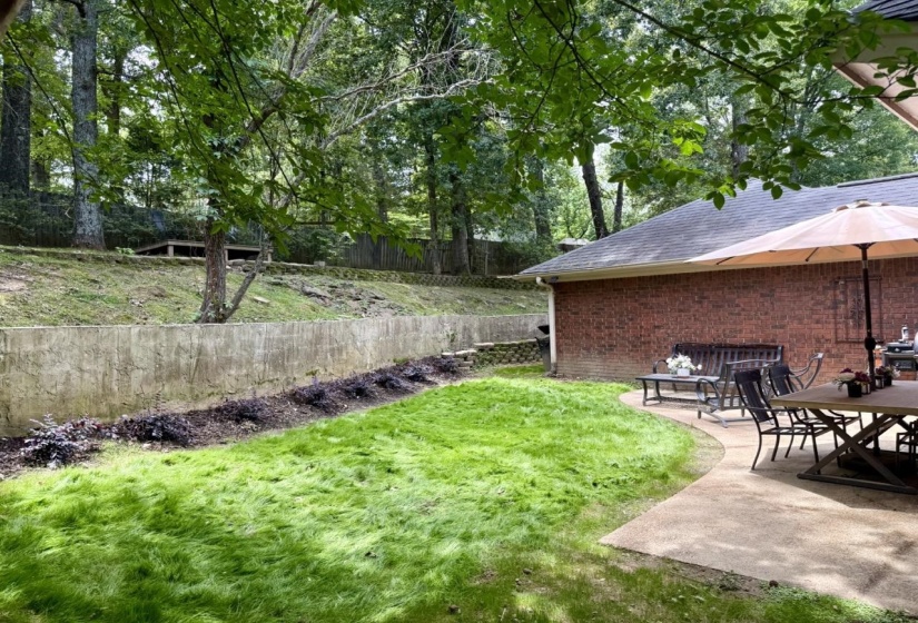 Expansive backyard featuring a concrete patio, brick exterior, and a retaining wall