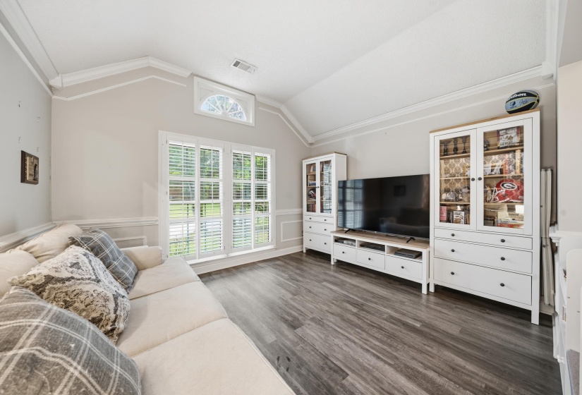 Vaulted ceiling with crown molding and a large window featuring plantation shutters