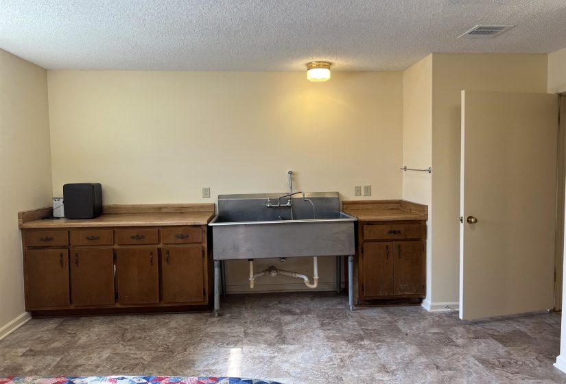 Kitchen with visible vents, baseboards, brown cabinetry, a textured ceiling, and a sink