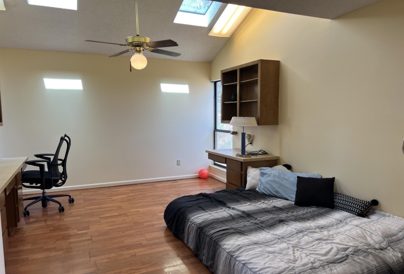 Bedroom with baseboards, lofted ceiling with skylight, ceiling fan, and light wood finished floors and built ins,