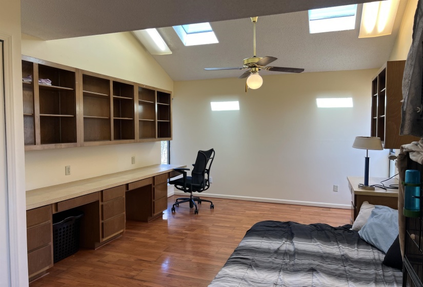Bedroom featuring ceiling fan, lofted ceiling with skylight, dark wood finished floors, and built in study area