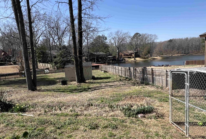 View of yard with a storage shed, a water view, an outdoor structure, and fence