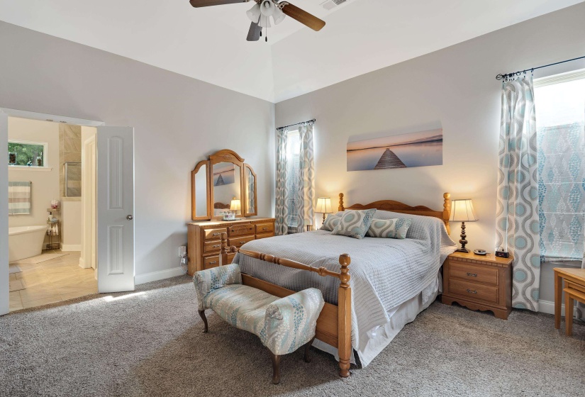 Spacious bedroom featuring vaulted ceilings, carpet flooring, a ceiling fan, and abundant natural light from multiple windows