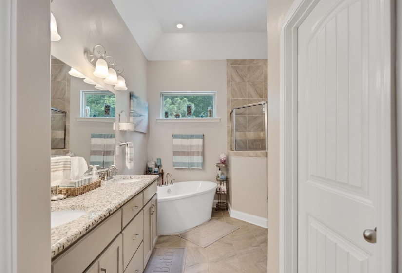 Bathroom featuring a dual vanity with a light-toned countertop, a soaking tub, and a separate tiled shower enclosure