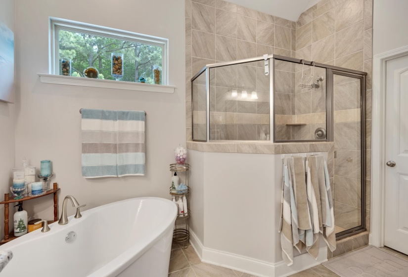 Freestanding soaking tub with brushed nickel fixtures, complemented by a glass-enclosed shower with tile surround and integrated shelving