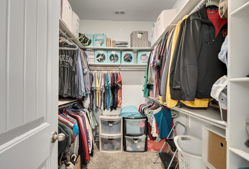 Walk-in closet featuring built-in shelving, multiple hanging rods, durable carpet flooring, and a ceiling light fixture