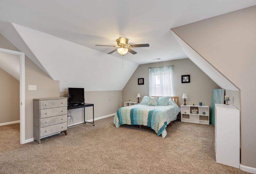 Carpeted room featuring sloped ceilings, a ceiling fan with integrated lighting, a window with sheer curtains, and neutral wall paint