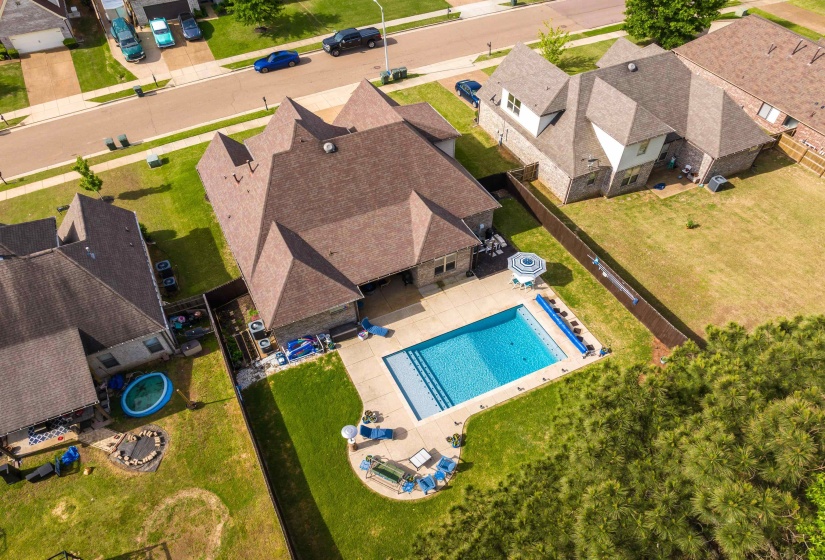 Rear exterior featuring a rectangular in-ground swimming pool with concrete surround, covered patio area, and a fenced backyard