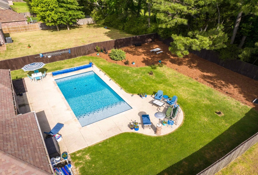 Expansive outdoor living area featuring a rectangular swimming pool with a pool cover, a surrounding concrete patio, and a fenced perimeter
