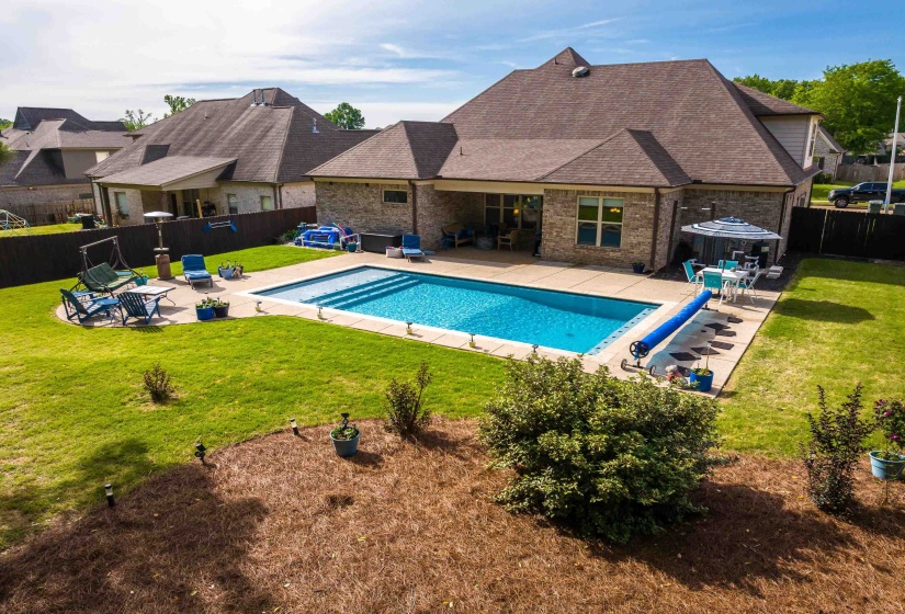 Expansive backyard featuring a rectangular in-ground swimming pool, concrete patio, and a manicured lawn