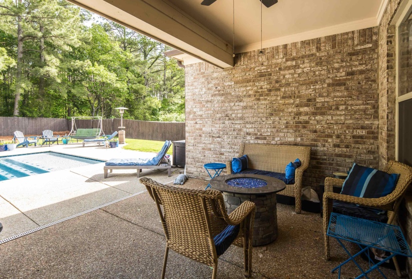 Covered patio with a brick accent wall, ceiling fan, and fire pit