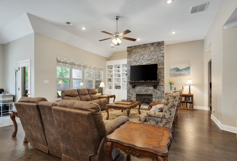 Living area featuring a stone-clad fireplace with a dark wood mantel, built-in shelving, vaulted ceilings, recessed lighting, and wood-finish flooring