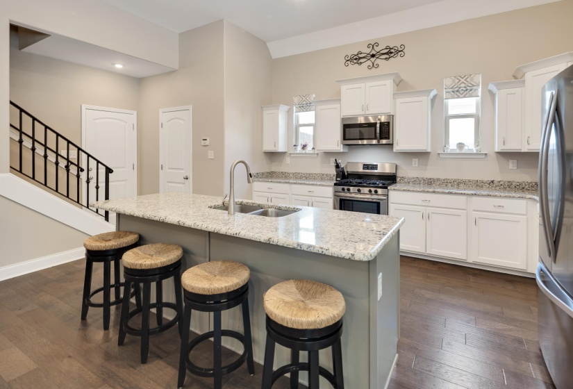 Kitchen featuring white cabinetry, light-toned countertops, a stainless steel range with microwave, and a central island with an undermount sink