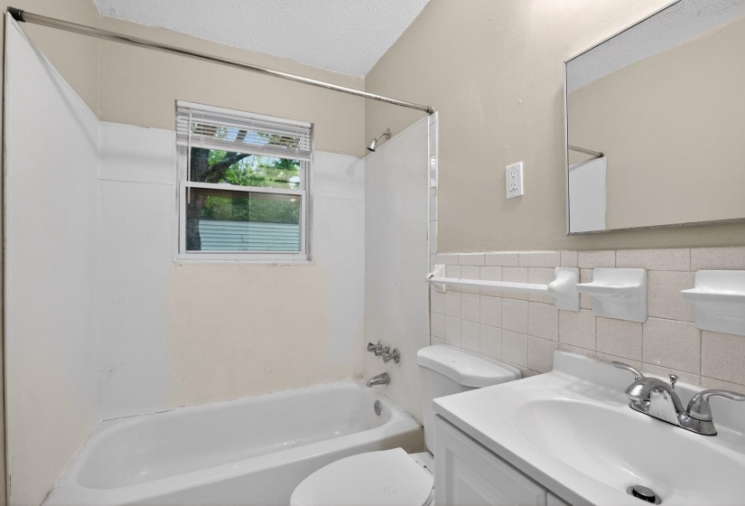 Bathroom featuring a white bathtub, small window, toilet, and vanity with a sink and chrome faucet