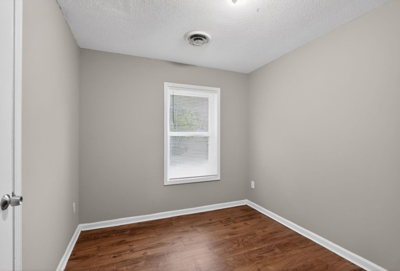 Interior room featuring wood-finish flooring, neutral wall paint, white trim, and a window with blinds