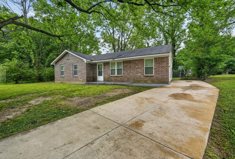 Brick exterior with a dark shingle roof, concrete driveway, and mature perimeter trees